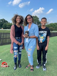 three people standing in a grassy field with a small dog