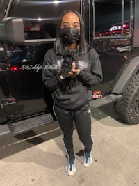 a woman wearing a face mask standing next to a black jeep
